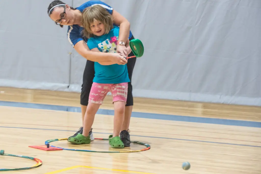 Instructor guiding child in playing indoor golf.