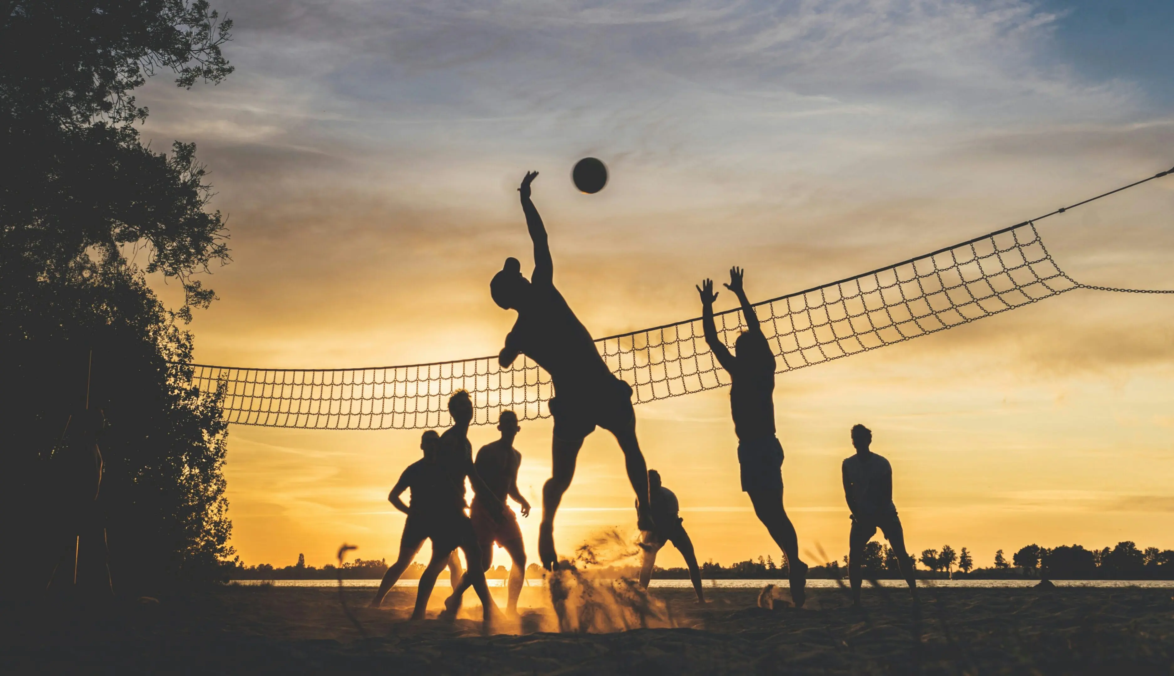 Silhouetted volleyball game at sunset beach.