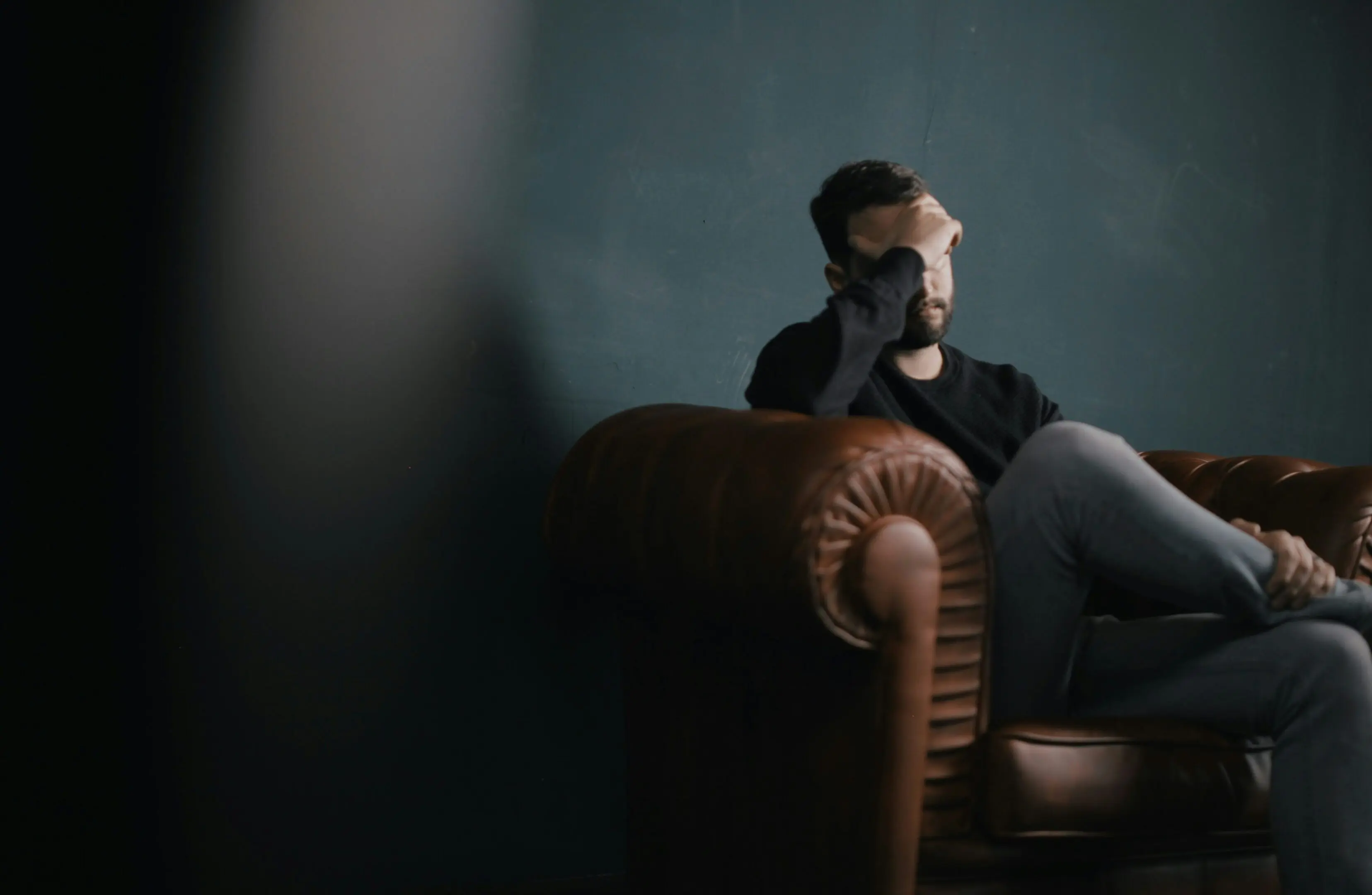 Man sitting on couch, looking thoughtful.