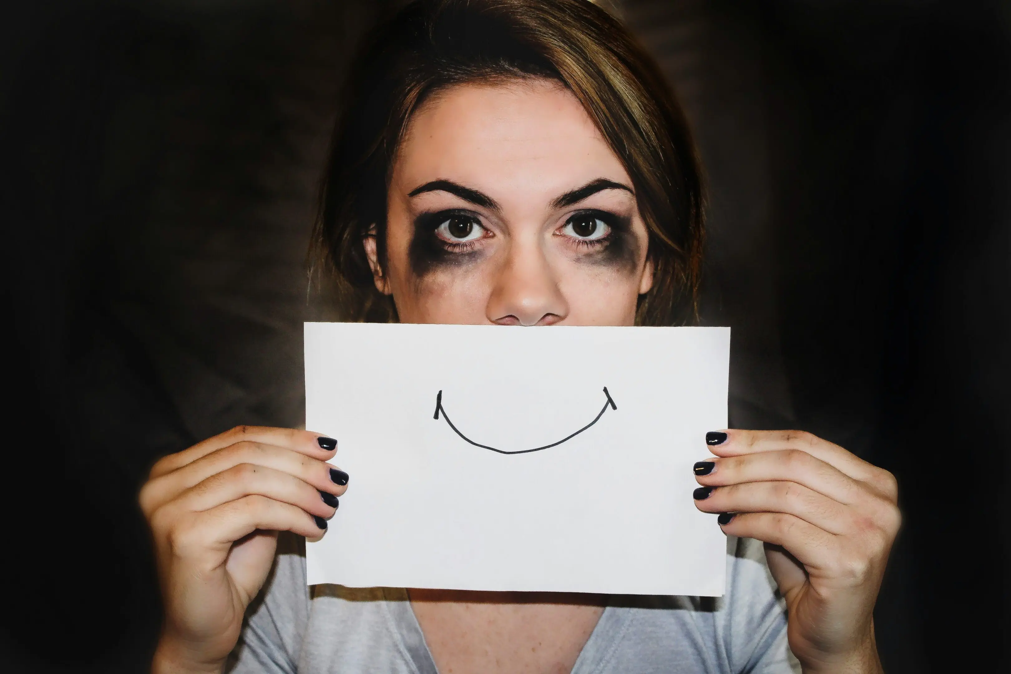 Woman holding paper with drawn smiley face.
